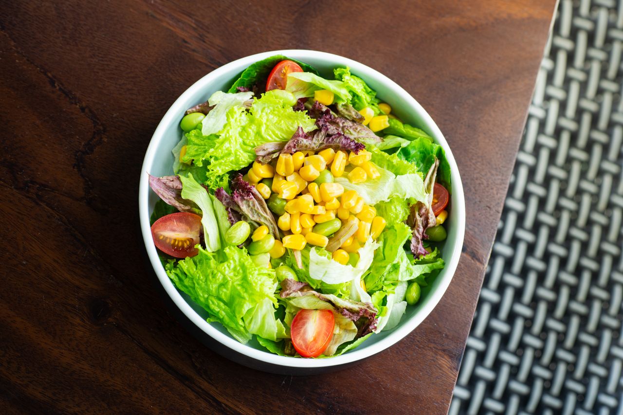 Home A vibrant salad with lettuce, cherry tomatoes, corn, and edamame in a white bowl.