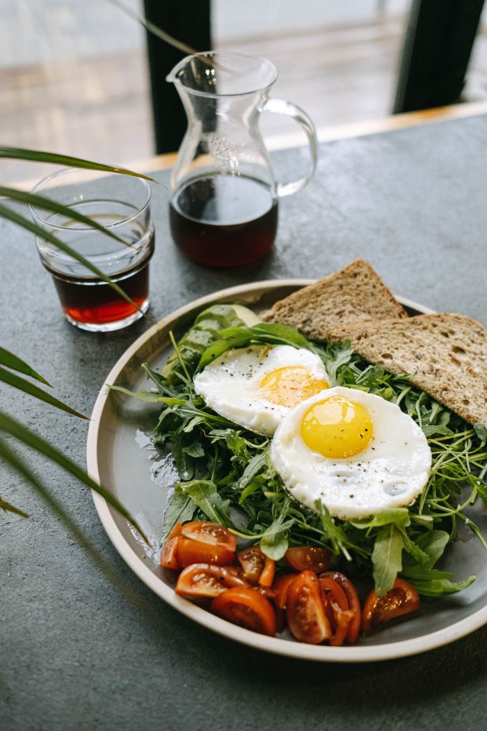 About Fresh breakfast plate with sunny-side-up eggs, salad, tomatoes, and rye bread.