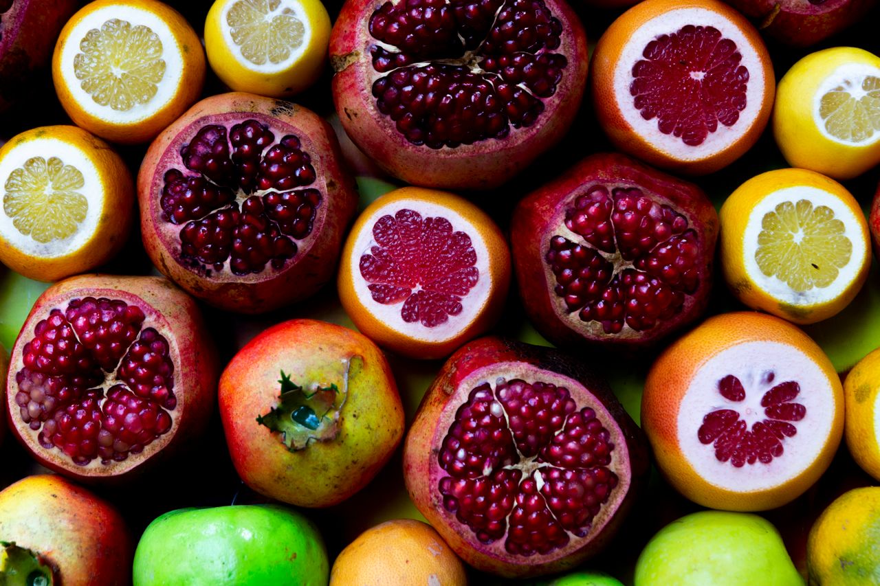 A colorful assortment of fresh fruits including pomegranates, lemons, and grapefruits.
